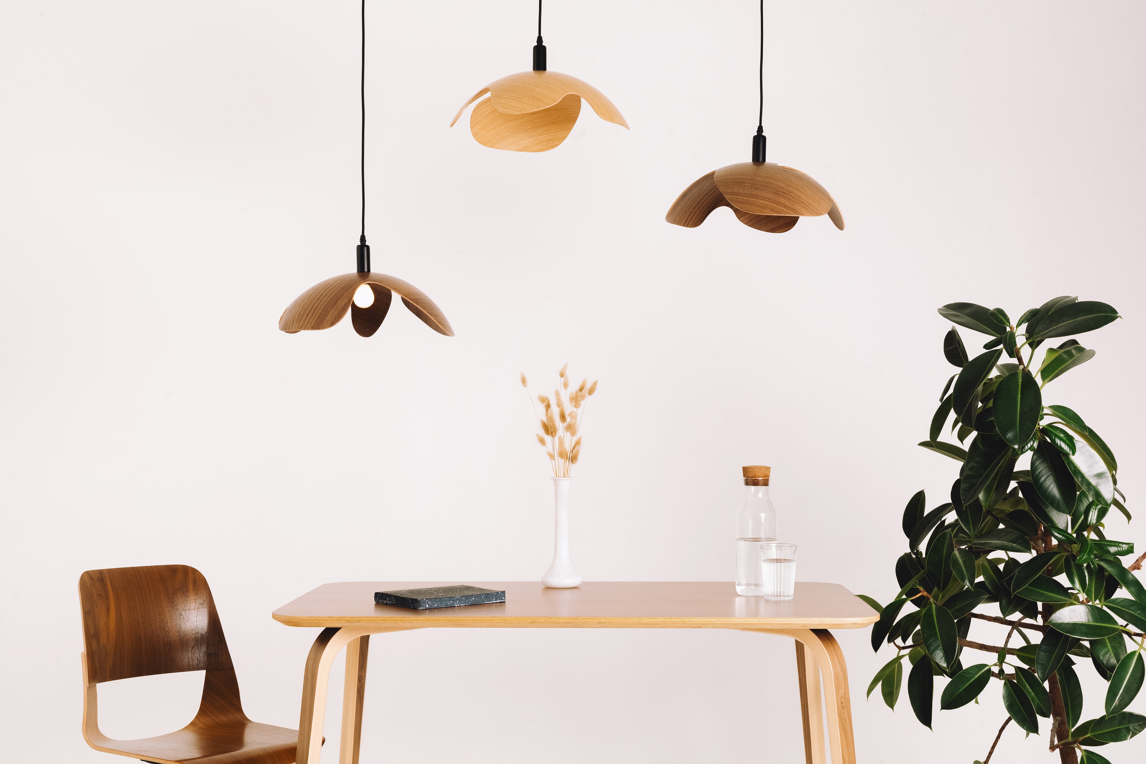 Modern dining area with wooden table, chairs, and pendant lights against a white wall.