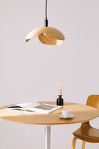 Wooden pendant lamp above a round wooden table with a book and cup on a light gray background