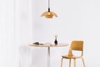 Minimalist dining setup with a round table and chair under a unique pendant light against a white background.