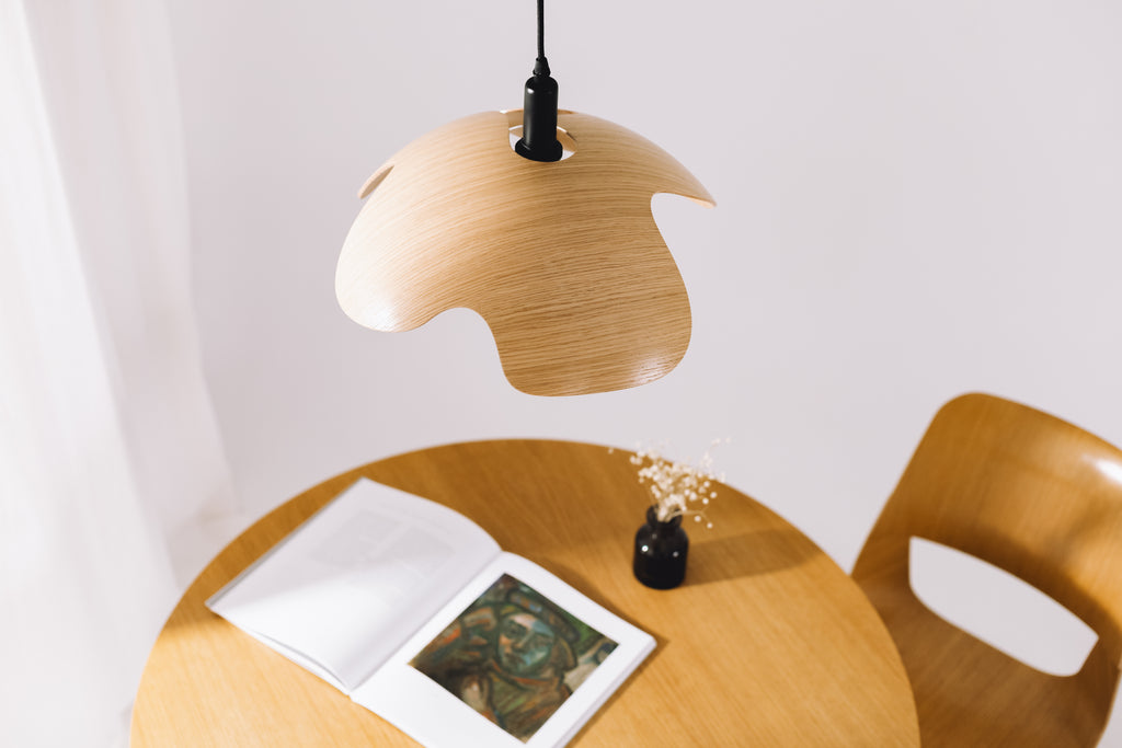 Wooden pendant lamp hanging above a round wooden table with an open book and a small black vase.