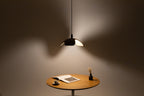 Pendant light illuminating a small round wooden table with a book and a cup on it.